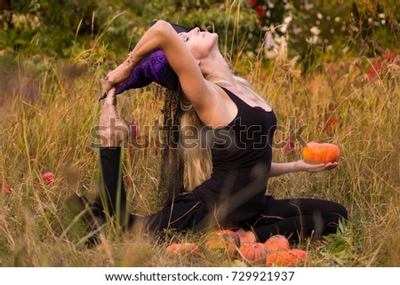 Happy woman in Halloween witch costume practicing yoga positions with pumpkins in her hands
