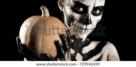 Isolated on black, wide-screen, closeup picture, young brunette caucasian pretty woman with scull body art with a pumpkin in hands, grey eyes, look at camera, wide opened eyes