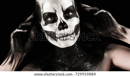 Isolated on black, closeup picture, beautiful young blonde caucasian woman with scull body art, wide open grey eyes, hands on the head, languid look