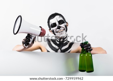 Isolated on white, closeup picture, young brunette caucasian pretty woman with scull body art holds green beer bottles and megaphone, grey eyes, cheerful, look at camera