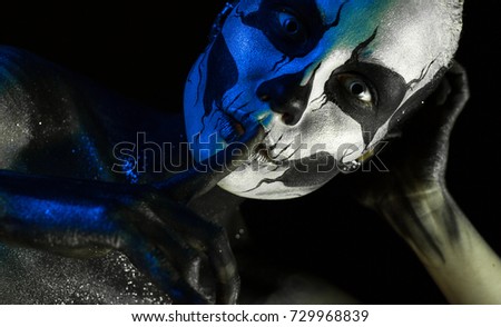 Isolated on black, closeup picture, toned white and blue, beautiful 
creepy young blonde caucasian woman with scull body art, grey eyes, hand on head, points to be silent