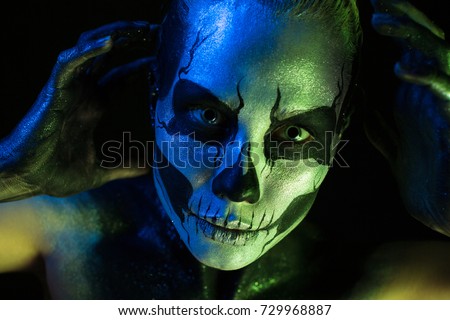 Isolated on black, closeup picture, toned green and blue, beautiful 
creepy young blonde caucasian woman with scull body art, grey eyes, hands on head