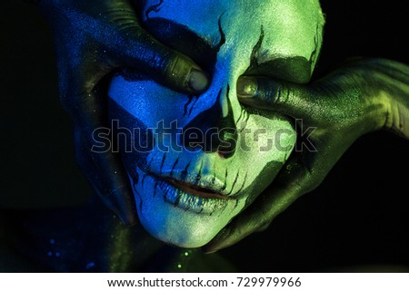 Isolated on black, closeup picture, toned green and blue, spooky young blonde caucasian pretty woman with scull body art, closed grey eyes, closes her eyes with her thumbs, half opened mouth