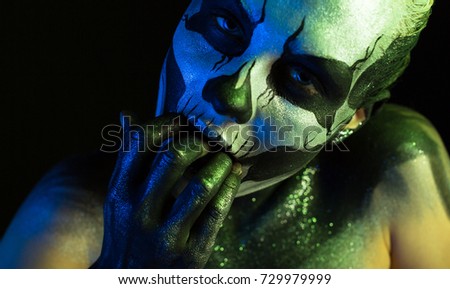 Isolated on black, closeup picture, toned green and blue, spooky young blonde caucasian pretty woman with scull body art, grey eyes, hand in her mouth, look at camera