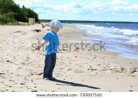 Little boy on sand beach drops stone to sea waves