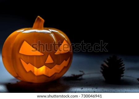 Halloween pumpkin head jack lantern on dark floor and background with silhouettes pinecone and dry leave on the floor.Halloween party concept.