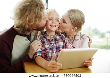 Affectionate parents kissing their cute daughter on cheeks while spending time together