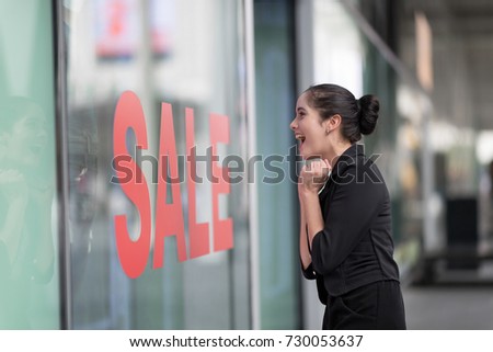 Woman excited looking into shop with shop window display with text SALE on red poster.Going shopping downtown concept