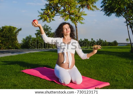 Pregnant woman choosing between a hamburger and apple. Pregnant yoga. Concept of healthy eating.