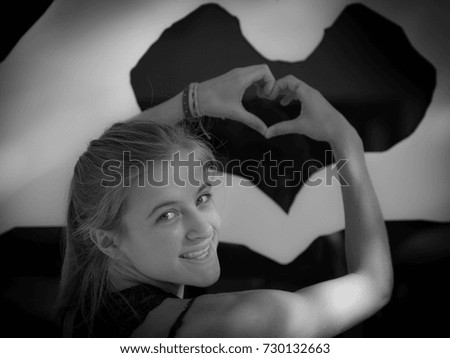 Smiling Female makes heart hand sign against wall art.
