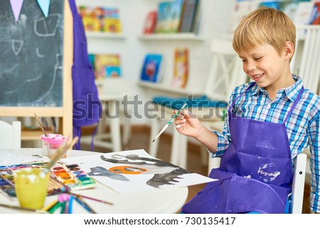 Portrait of cute little boy  smiling while painting Halloween picture sitting at table in art class