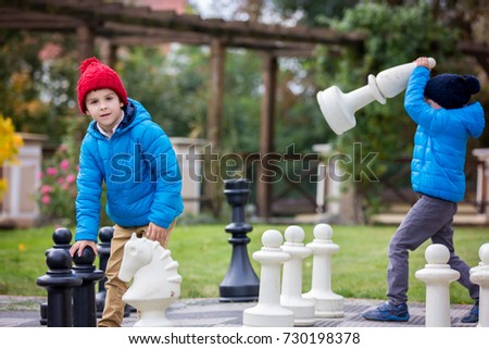 Two children, boy brothers, playing chess with huge figures in the park on the ground, autumn time. Childhood happiness concept, kids playing in the park fall time