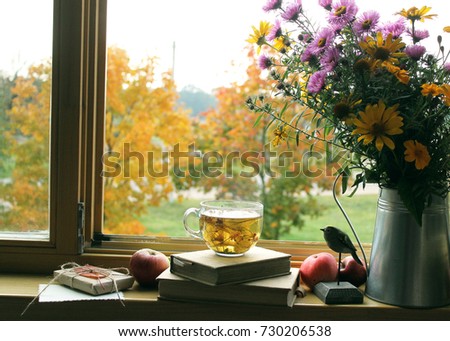 autumn background / bouquet of  flowers , a cup of tea , wooden bird and  books on the windowsill