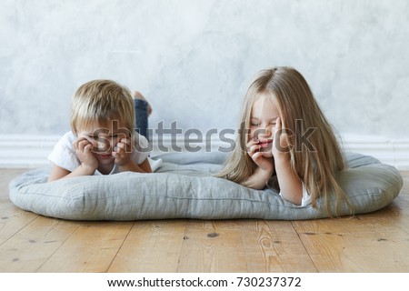 Picture of two preschool girls lying on mat in kindergarten, feeling bored. Cute female child resting on floor at home together with her baby sister, telling fairy tales. Childhood and relationships