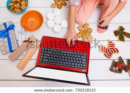 Creative leisure time on New Year's day. Unrecognizable girl watching Christmas cartoons, laptop with white screen mockup. Festive decorations on wooden background top view