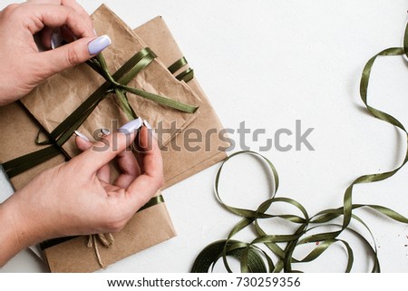 Holiday background of preparing eco presents. Small elegant gifts on white table with decorative ribbons are taped by unrecognizable woman, top view picture with free space