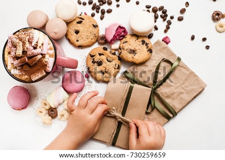 Christmas gifts and surprises from children. Little child preparing small presents for parents with cocoa and colorful macaroons, zephyrs and chocolate scones nearby. Top view picture