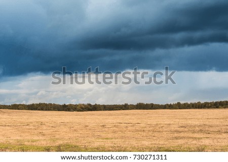 autumn landscape with cloudy weather, large rainy clouds over a chamfered yellow field, nature background