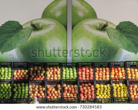 Apples of different colors, kinds and varieties (red, green, yellow) for sale on a market in Serbia, with a giant picture of apples in the background
