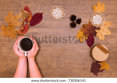 Fall coffee in warm scarf hugs on the wood table with dried maple leaves and gingerbread