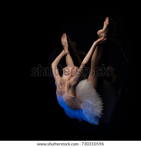 Girl ballerina posing and performing dance elements in blue scenic light on a black background