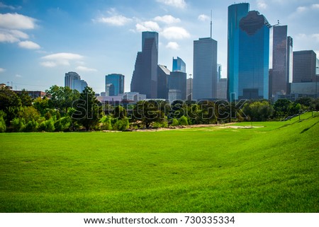 Bright Green Grass and Large open field in front of Downtown Houston , Texas along the Buffalo Bayou River Park lined with trees and tall Skyscrapers 