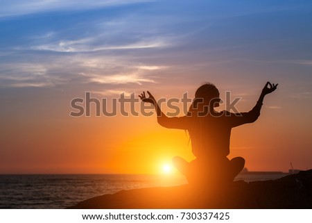 Silhouette of young woman practicing yoga on the sea beach during amazing sunset.