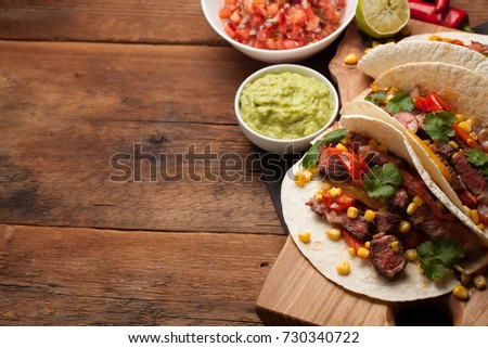 Three Mexican tacos with marbled beef, black Angus and vegetables on old rustic table. Mexican dish with sauces guacamole and salsa in bowls. Top view with copy space.