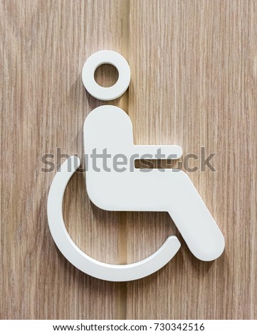 Disable person sign for restroom in white against wooden background. Toilet icon for handicap.