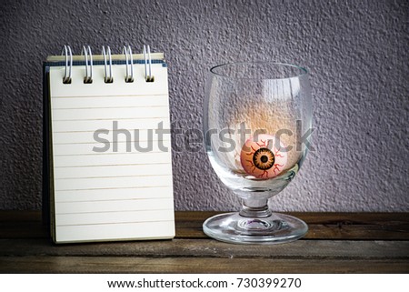 notepad with eye ball in glass on wood and wall background. Using wallpaper or background for halloween day image.