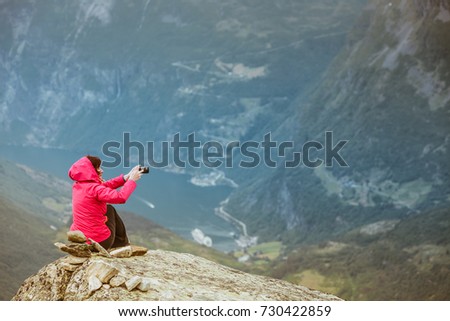 Tourism vacation and travel. Female tourist taking photo with camera, enjoying Geiranger fjord and mountains landscape from Dalsnibba Plateau viewpoint, Norway Scandinavia.