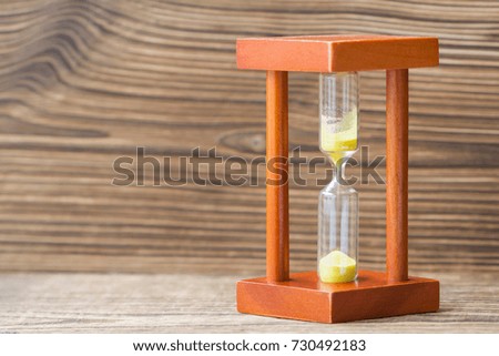 Time passing concept. Hourglass with yellow sand on wooden background.