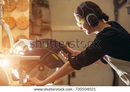 Attractive female carpenter using some power tools for her work in a woodshop Royalty-Free Stock Photo #730504021