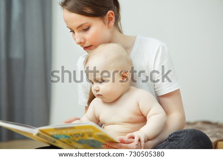 Mother reading to little infant colorful book with fairy tales. little toddler listens attentively to his mom and watch pictures in textbook