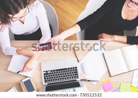 Top view of two businesswoman at workplace handing credit card to colleague