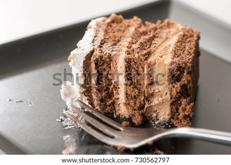 Slice of chocolate cake on the black plate with metal fork.