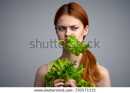 young woman eating salad leaves on gray background portrait, vegetable diet                               