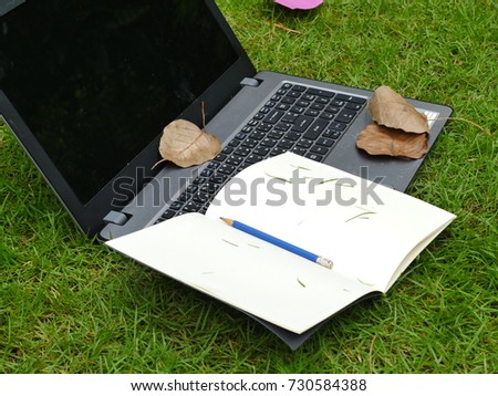 Blank book and laptop on green glass background. 