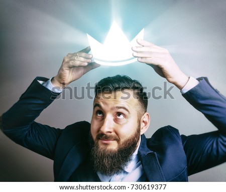 The image of a man in a suit that puts a luminous royal crown on his head. The concept of careerism, achieving the goal, smugness, egoism, success and etc. Royalty-Free Stock Photo #730619377
