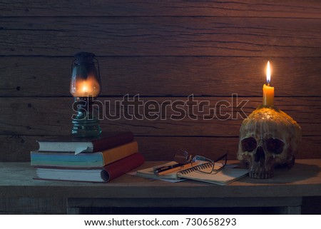 Lantern light on books and Skull with candle light on head all  is on the wooden plank / Still Life Image

