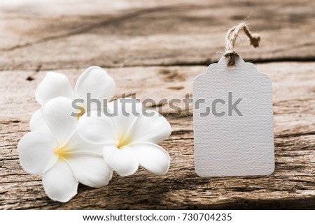 White paper tag label decorate with plumeria flowers on rustic wood table