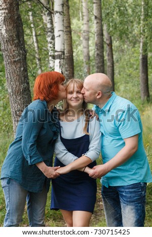 Happiness and harmony in family life. Happy family concept. Mother and father kissing their daughter in the park. . Family having fun outdoor