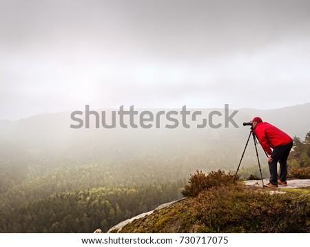 Photographer looking into viewfinder of dslr digital camera stand on tripod. Artist  photographing mountain and cloudy landscape.  Man check picture on screen his camera while shooting nature pictures