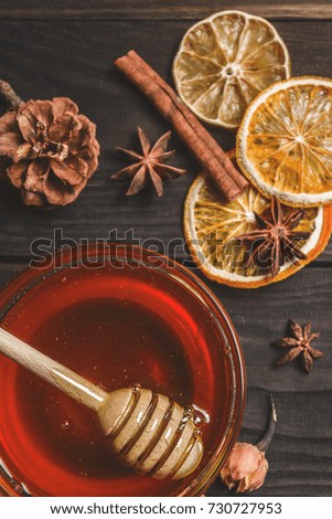 Ingredients for mulled wine. Fresh golden honey in a glass bowl with a wooden spoon for honey on a wooden background. Dried citrus, cinnamon and star anise are scattered on the table. Holiday mood