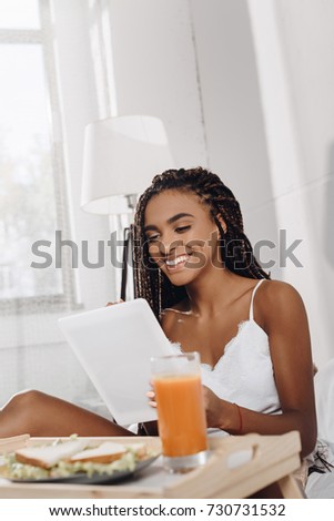 african american woman with breakfast in bed using tablet