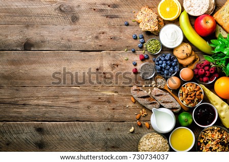 Healthy breakfast ingredients, food frame. Granola, egg, nuts, fruits, berries, toast, milk, yogurt, orange juice, cheese, banana, apple on wooden rustic background, top view, copy space