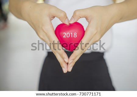 Close up woman hand making sign as heart shape while holding red heart rubber ball for love with letter 2018. Health care, life insurance and relationship, Happy new year 2018. Royalty-Free Stock Photo #730771171