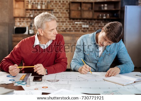 Senior man supervising young colleague drawing blueprint