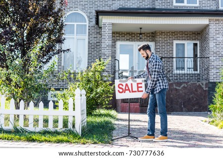 young man with sale board selling his house Royalty-Free Stock Photo #730777636