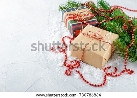Christmas gift boxes in kraft paper, red glass beads and fir branches on a snow-covered background